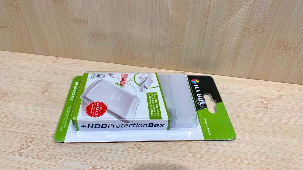 Eine weiß-grüne Verpackung inklusive eines weißen 2,5-Zoll-Festplattengehäuses im Test auf einer Holzoberfläche.
