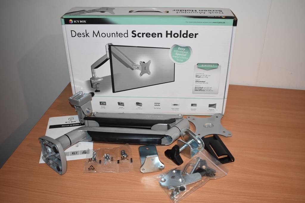 Eine Monitorhalterung mit Karton, Schrauben und Kabeln auf einem Holztisch.