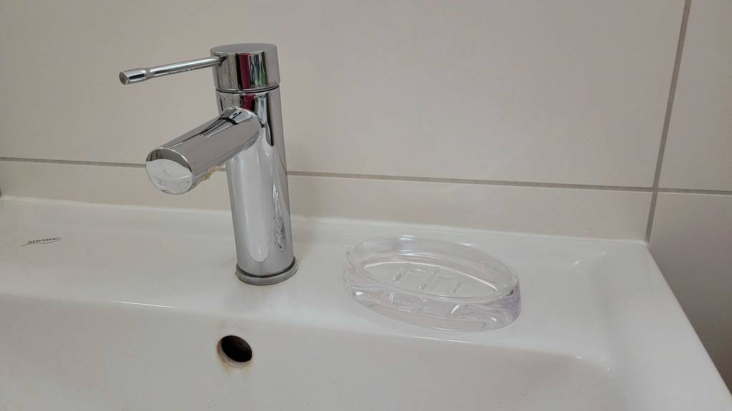 Seifenschalen-Test: Eine transparente Seifenschale steht auf einem weißen Waschbeckenrand neben einem verchromten Wasserhahn.