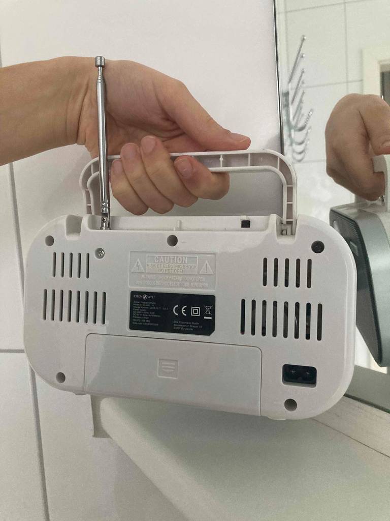 Rückansicht eines getesteten Kofferradios: Hand hält das Radio am Griff vor einem Spiegel.