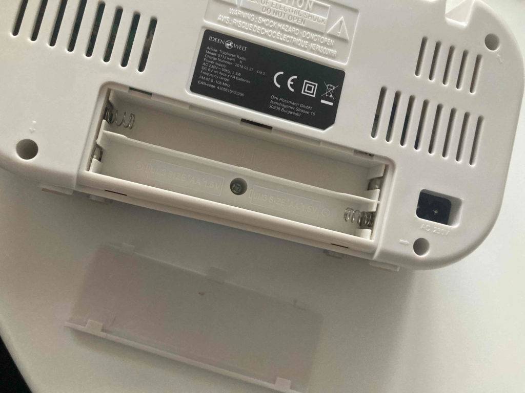 Detailansicht der Rückseite eines weißen, getesteten Kofferradios mit Fokus auf das geöffnete Batteriefach.