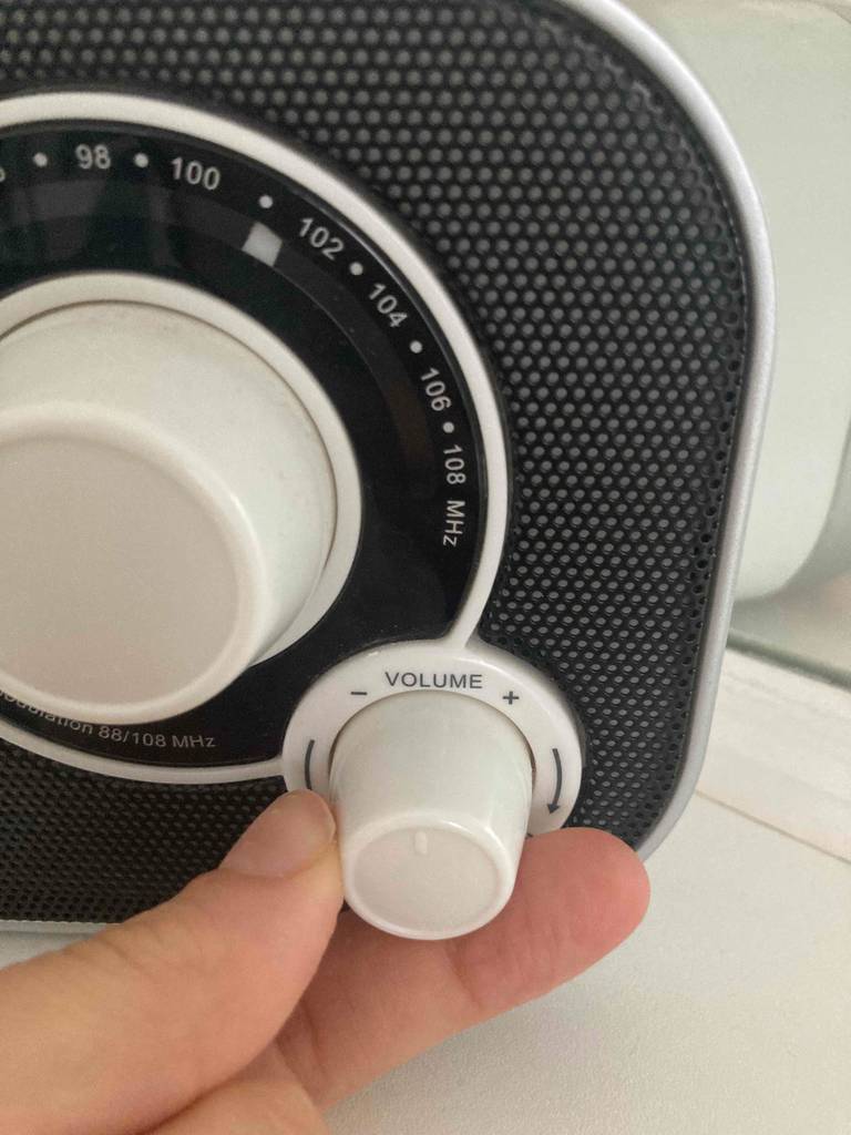 Detailansicht eines Kofferradios im Test: eine Hand reguliert die Lautstärke am Drehknopf neben dem Sendersucher.