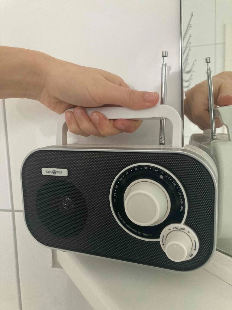 Vorderansicht eines Kofferradios im Test: eine Hand stellt das Modell Ideenwelt am Griff auf ein Regal.