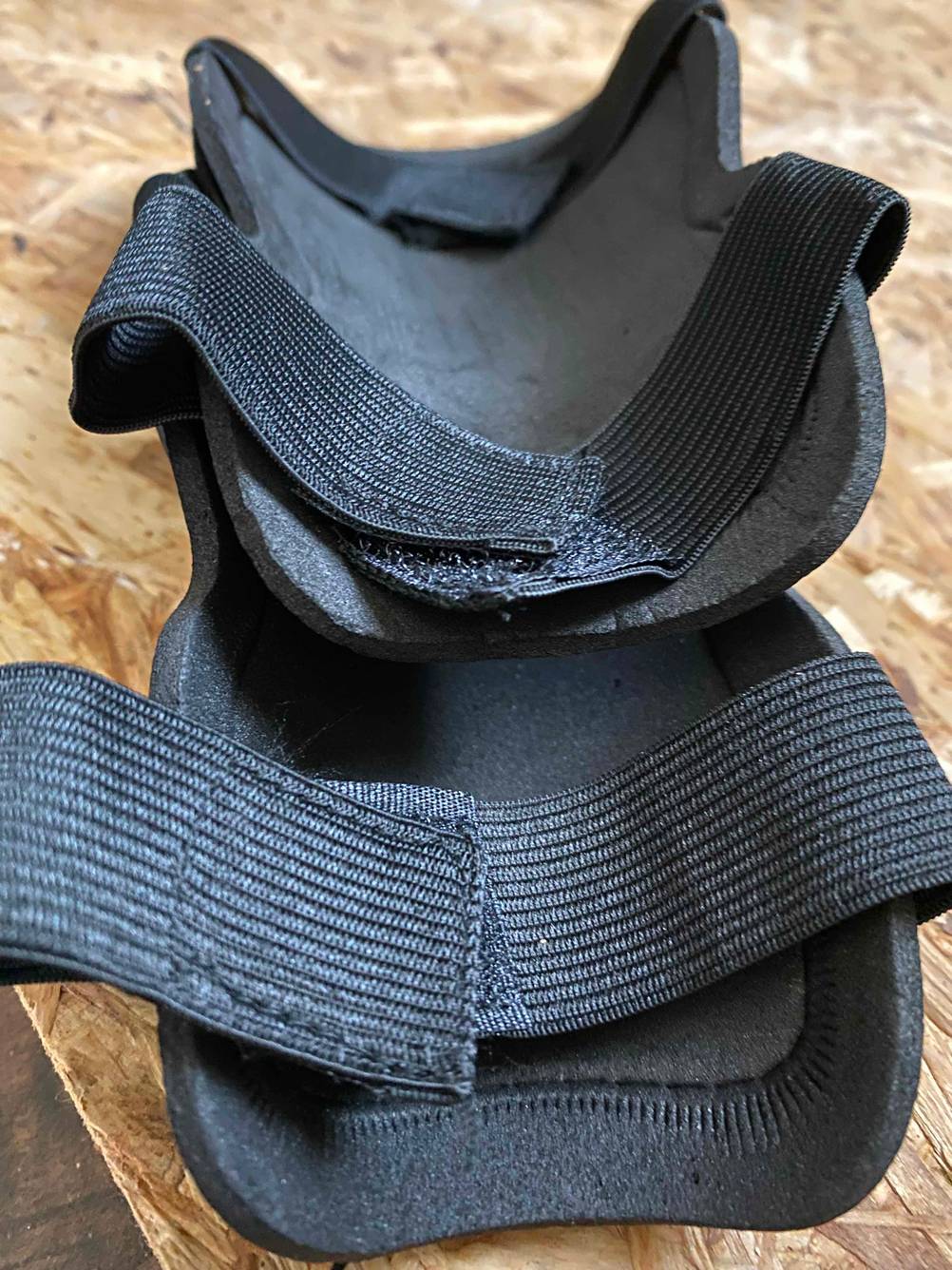 Zwei schwarze getestete Schienbeinschoner auf Holzboden, mit Sicht gepolsterter Rückseite inklusive elastischen Klettverschlüssen.