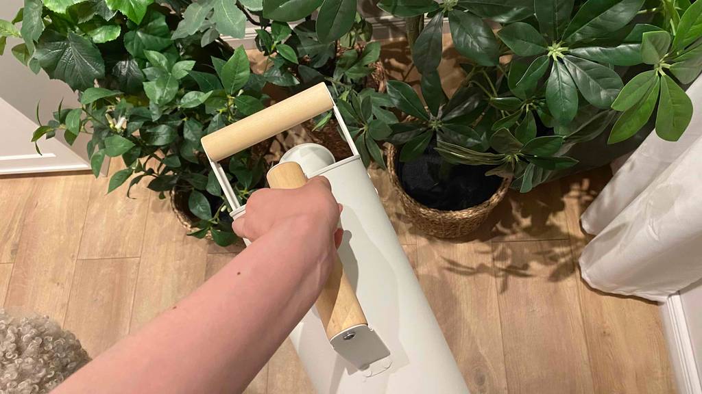 Eine Hand hält den Holzgriff einer getesteten Gießkanne in Weiß und wässert Topfblumen.