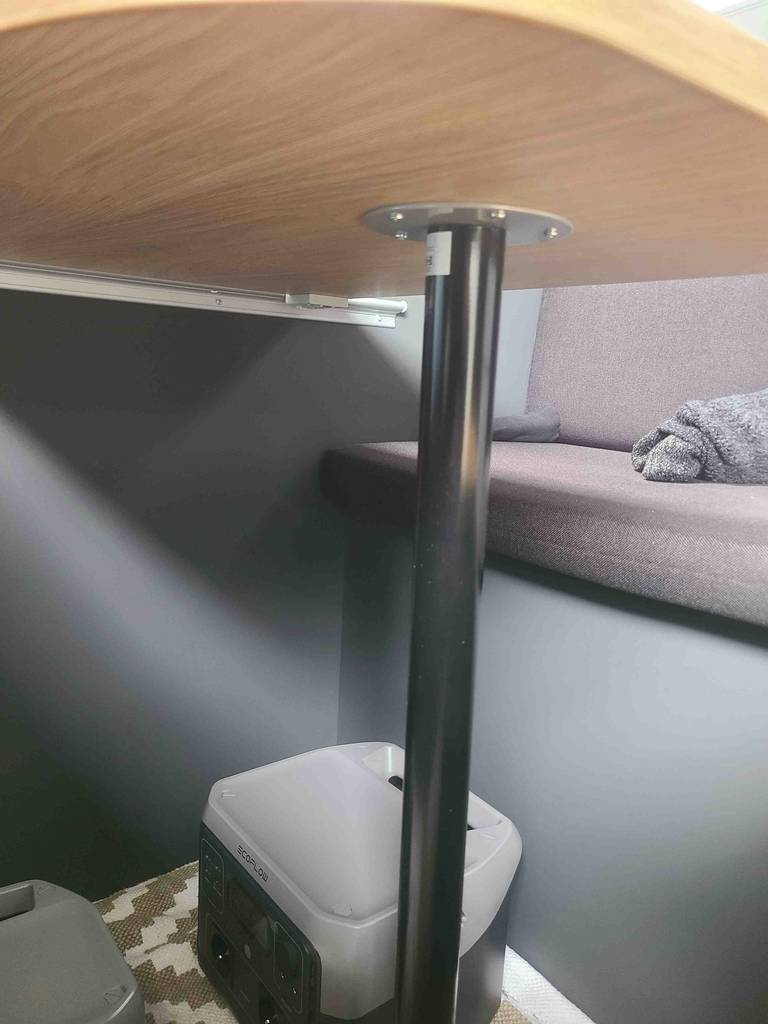 Das schwarze getestete Metall-Tischbein ist an der Unterseite eines Holztisches montiert.