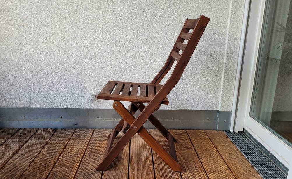 Gartenstühle getestet: Seitenansicht eines aufgeklappten Stuhls aus Holz der auf einem Balkon steht.