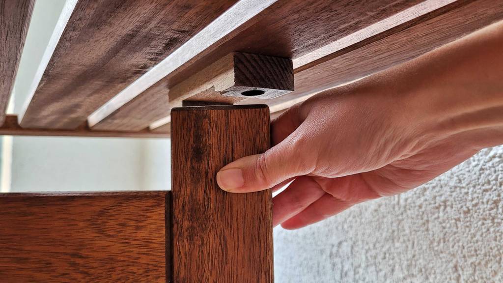 Getesteter Gartentisch aus Holz: Nahaufnahme einer Hand, die ein Standbein in die vorgesehene Position rückt.