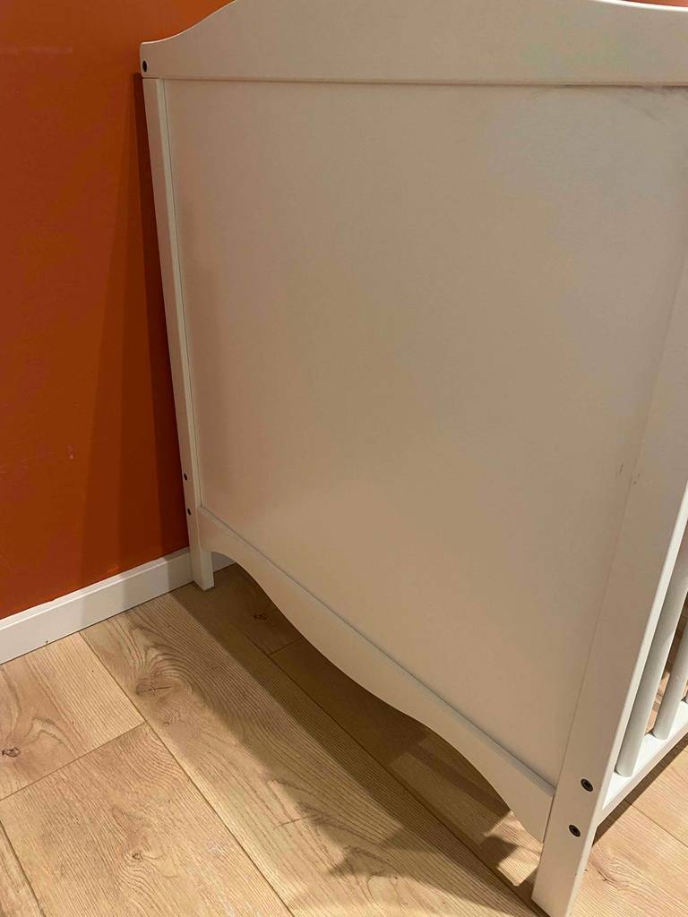 Nahaufnahme der Seitenwand eines getesteten Babybettes auf einem Holzboden.