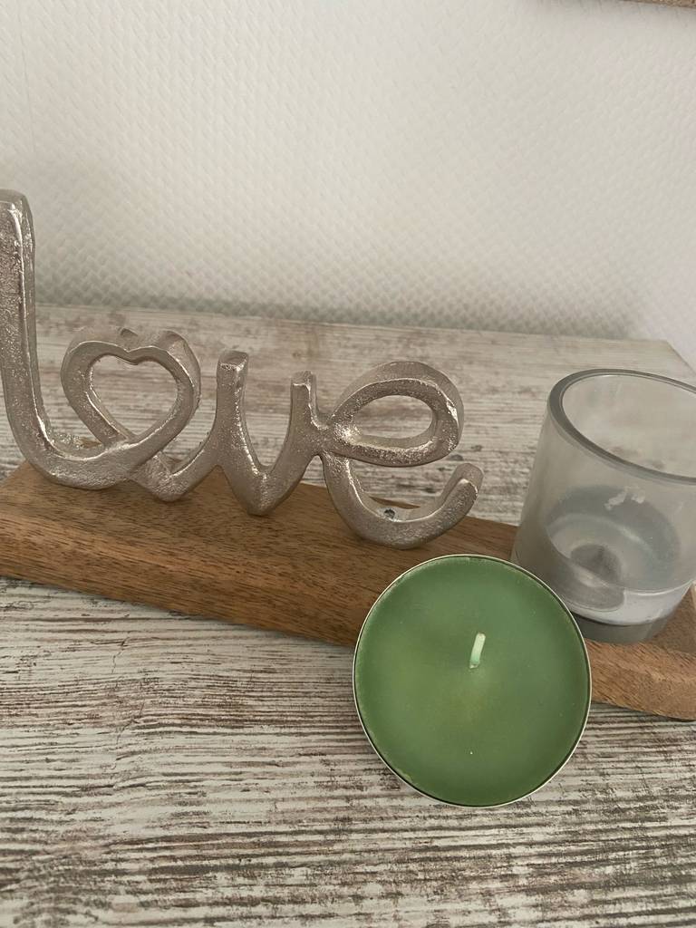 Duft-Teelichter getestet: Ein Teelicht steht vor einem in einem Glas abgebrannten Licht neben einem Love-Dekoartikel.