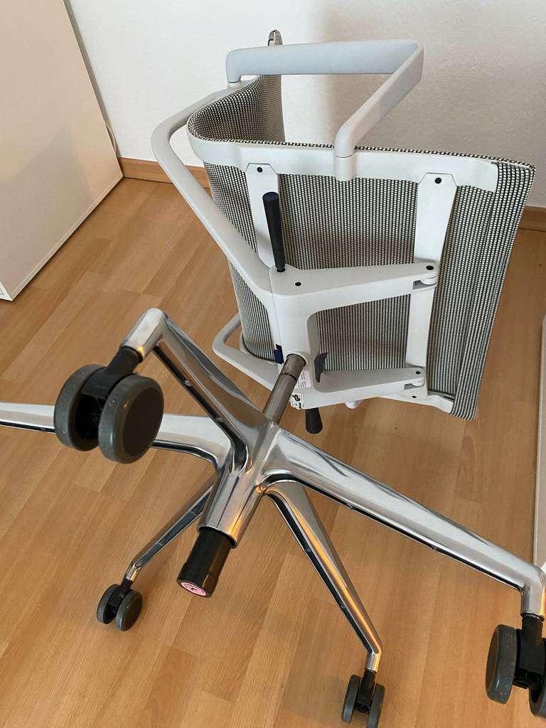 Ein heller ergonomischer Bürostuhl im Test ausgestattet mit einem weißgrauen Textilgewebebezug liegt auf einem Holzboden.
