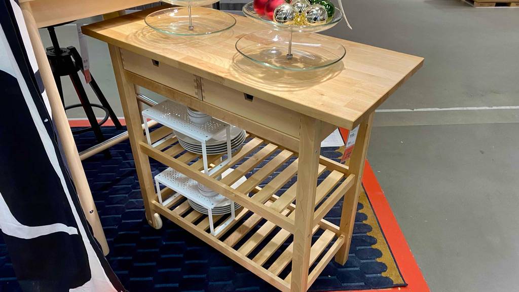 Servierwagen-Test: Ikea-Modell aus natürlichem Holz mit zwei Ablageflächen, zwei Schubladen und einer Tischablage inklusive Geschirr befindet sich in einem Ausstellungsbereich.