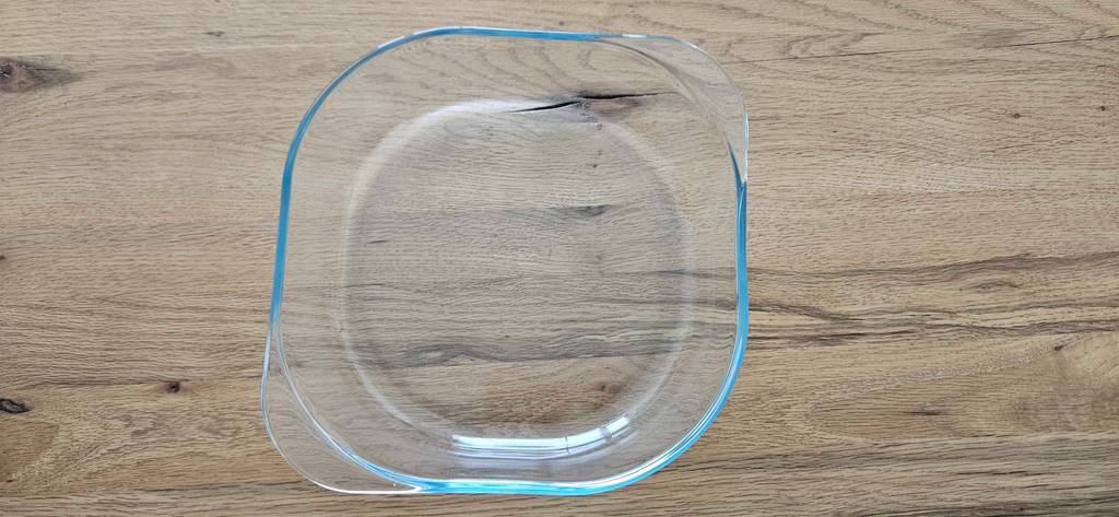 Ansicht von oben auf eine quadratische getestete Glas-Auflaufform mit abgerundeten Ecken und zwei Griffen, die auf Holz steht.