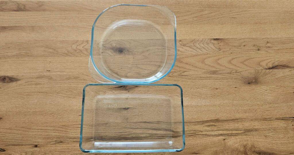 Ansicht von oben auf eine quadratische Glas-Auflaufform mit abgerundeten Ecken, die neben einer rechteckigen Glas-Auflaufform im Test auf einer Holztischplatte steht.