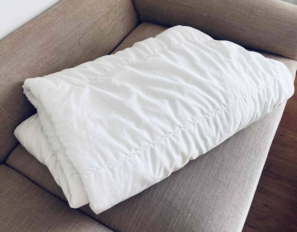 Weiße, gesteppte Bettwäsche im Test liegt zusammengefaltet auf einem beigefarbenen Sofa.