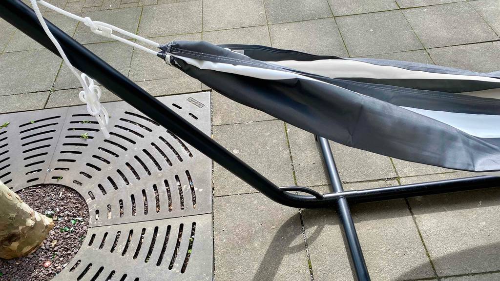 Detailansicht der grau-weiß gestreiften Liegefläche, die zu einer Hängematte mit Gestell im Test gehört, die im Außenbereich auf grauen Steinfliesen steht.