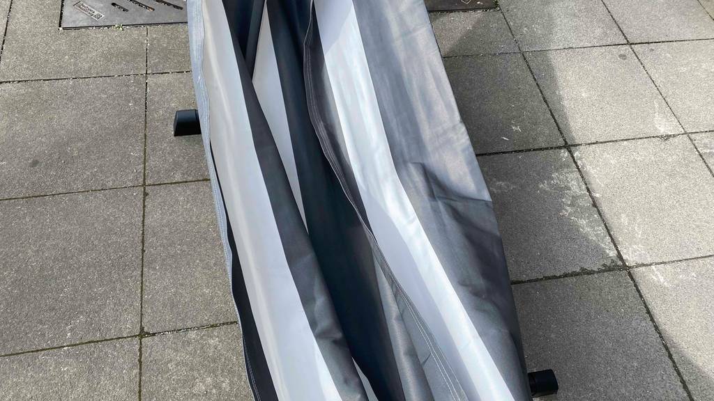 Detailansicht der grau-weiß gestreiften Liegefläche von einer getesteten Hängematte mit Gestell aus Metall, die im Außenbereich auf grauen Steinfliesen im Verkauf ausgestellt ist.
