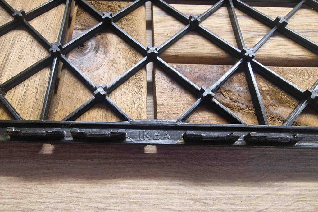 Nahaufnahme der Rückseite inklusive schwarzer Klick-Basis einer gestreiften getesteten Balkon-Holzfliese der Marke Ikea.