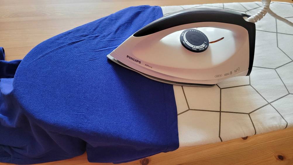 Im Test: Auf einem Tischbügelbrett wird mit einem Bügeleisen ein blaues Kleidungsstück gebügelt.