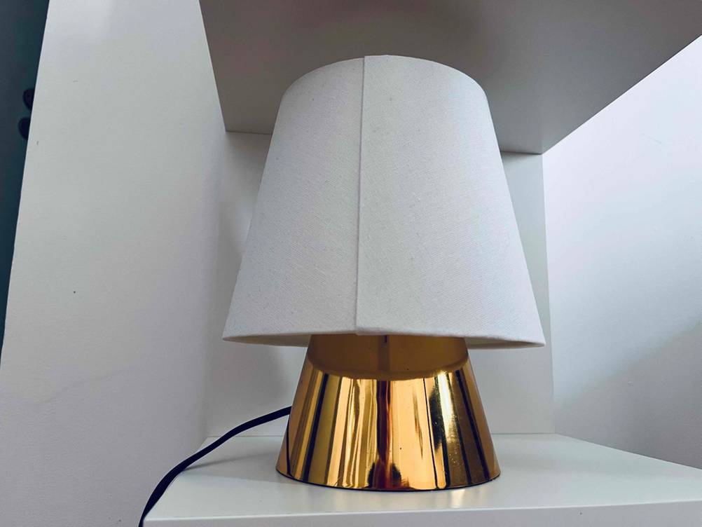 Eine Kinder-Schreibtischlampe im Test steht inklusive Messingfuß auf einem hellen Regal.