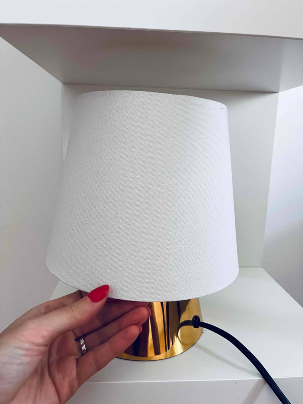 Hand greift nach dem hellen Lampenschirm einer getesteten Kinder-Schreibtischlampe mit Messingfuß.