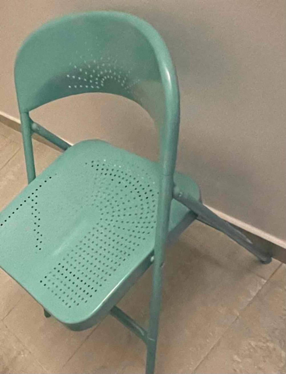 Seitenansicht von oben Ansicht von vorn auf einen geöffneten grünen Klappstuhl im Test, der vor einer weißen Wand steht.