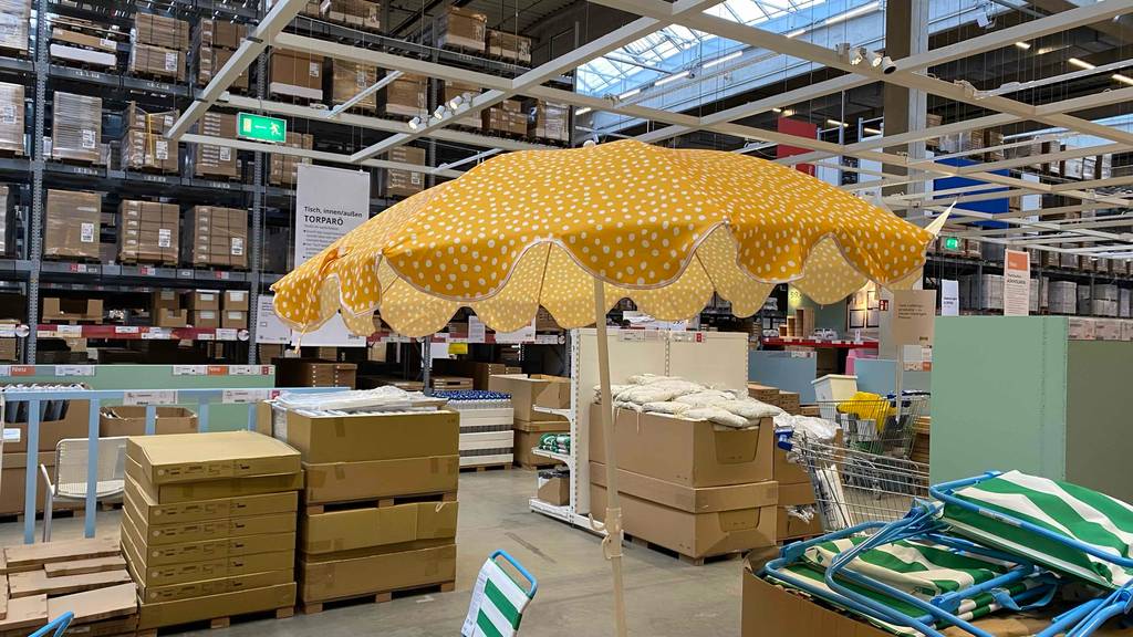 Ein aufgespannter gelber kleiner Sonnenschirm mit weißen Punkten steht zum testen in einer großen Verkaufshalle.