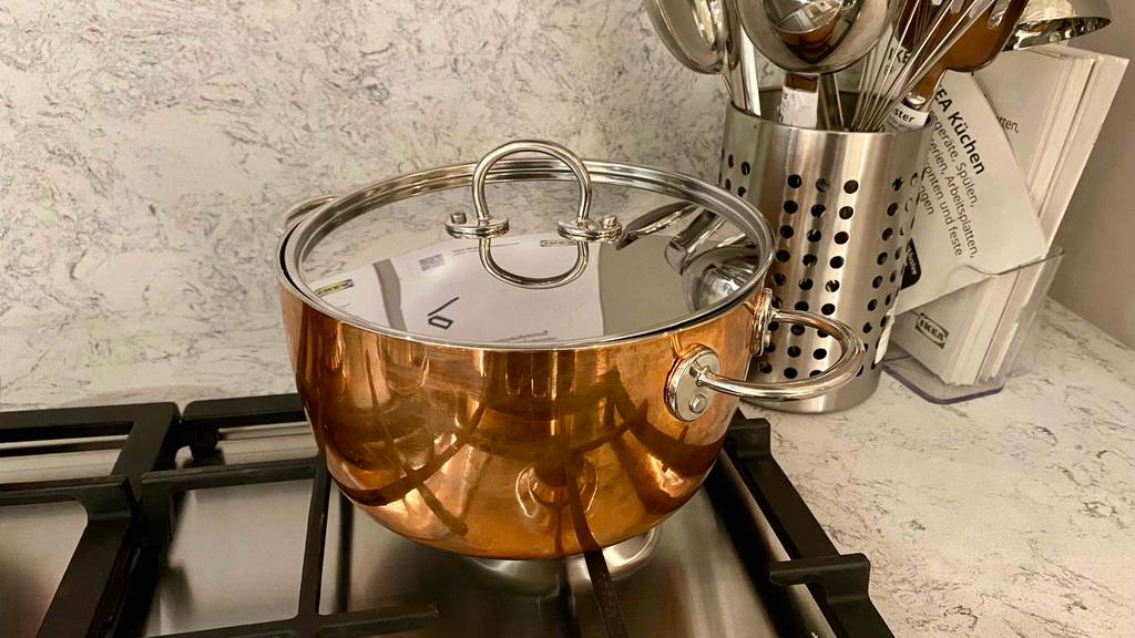 Ein getesteter Kupfertopf steht mit Deckel auf einem Gasherd.