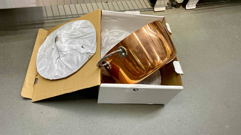 Im Test: Ein Kupfertopf liegt neben dem in Papier verpackten Deckel in der Originalverpackung.