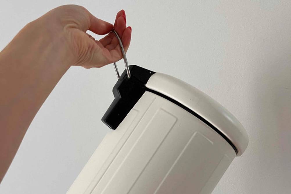 Im Test: Hand hält einen weiß-schwarzen Mülleimer am Henkel vor weißer Wand.