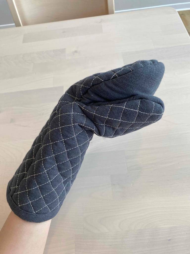 Eine Hand hat einen grauen getesteten Ofenhandschuh übergestülpt.