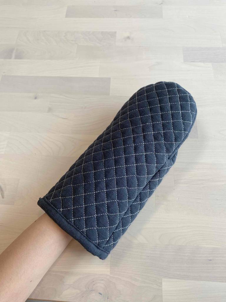Eine Hand mit einem übergestülpten Ofenhandschuh im Test befindet sich über einer weißen Fläche.