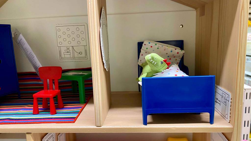 Puppenhaus im Test: Detailansicht von vorn auf zwei Zimmer eines Holzpuppenhauses inklusive blauem Bett und rotem Stuhl.