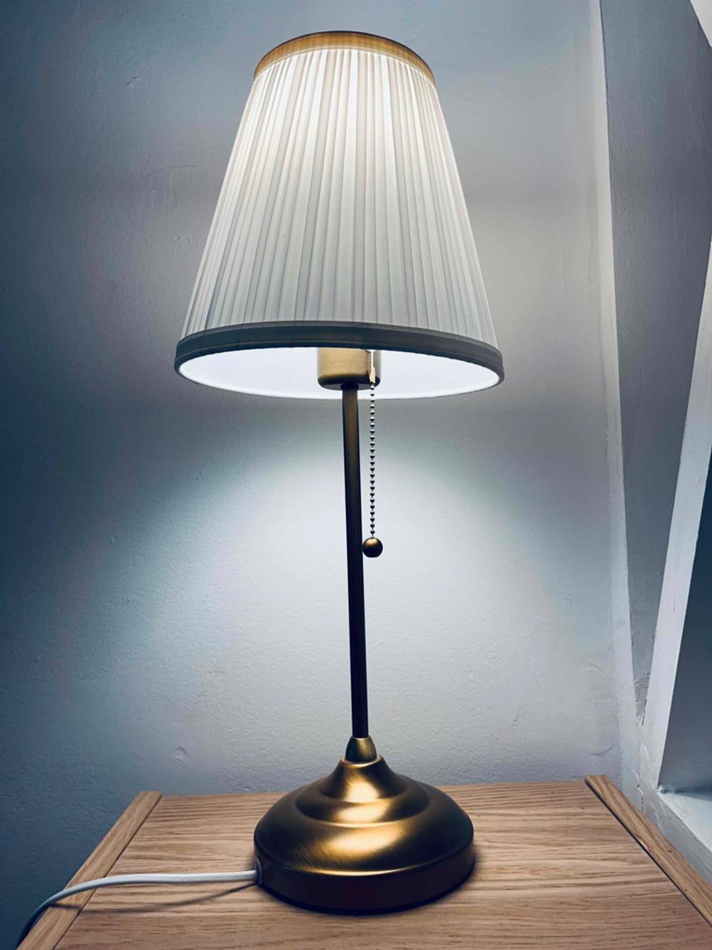 Im Test: Eine angeschaltete Schreibtischlampe auf einer Holzfläche vor einer hellen Wand.