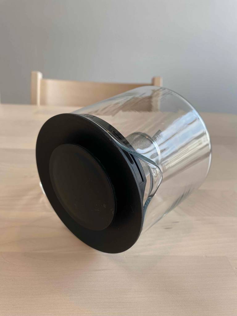 Eine getestete Teekanne aus Glas mit integriertem Filter liegt auf einem beigefarbenen Tisch.