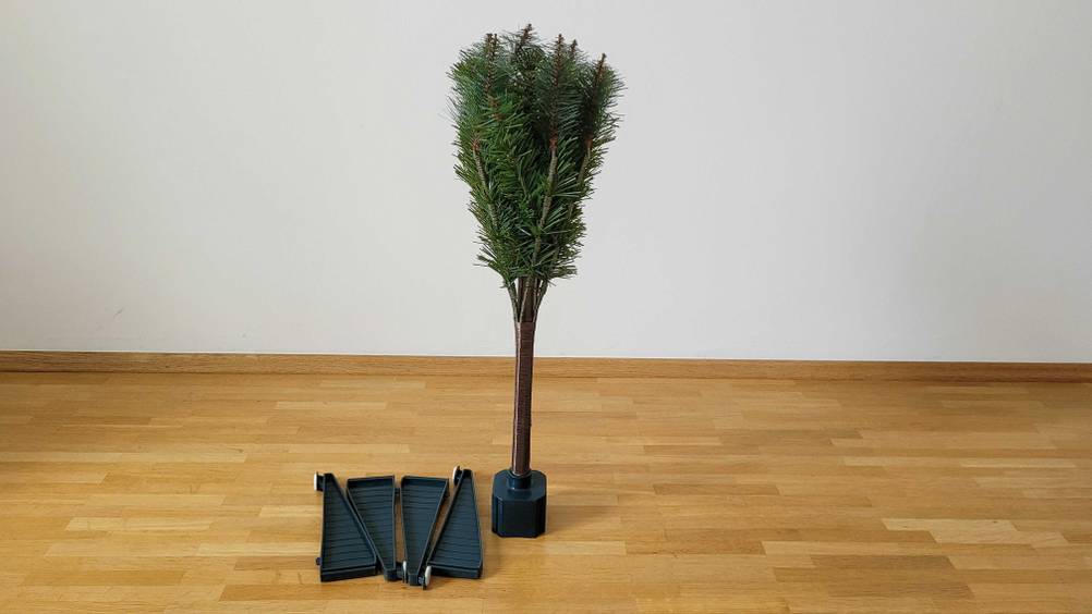 Künstlicher Weihnachtsbaum im Test: ein zusammengefalteter Weihnachtsbaum steht in einem halb aufgebauten Ständer neben den Standfüßen.