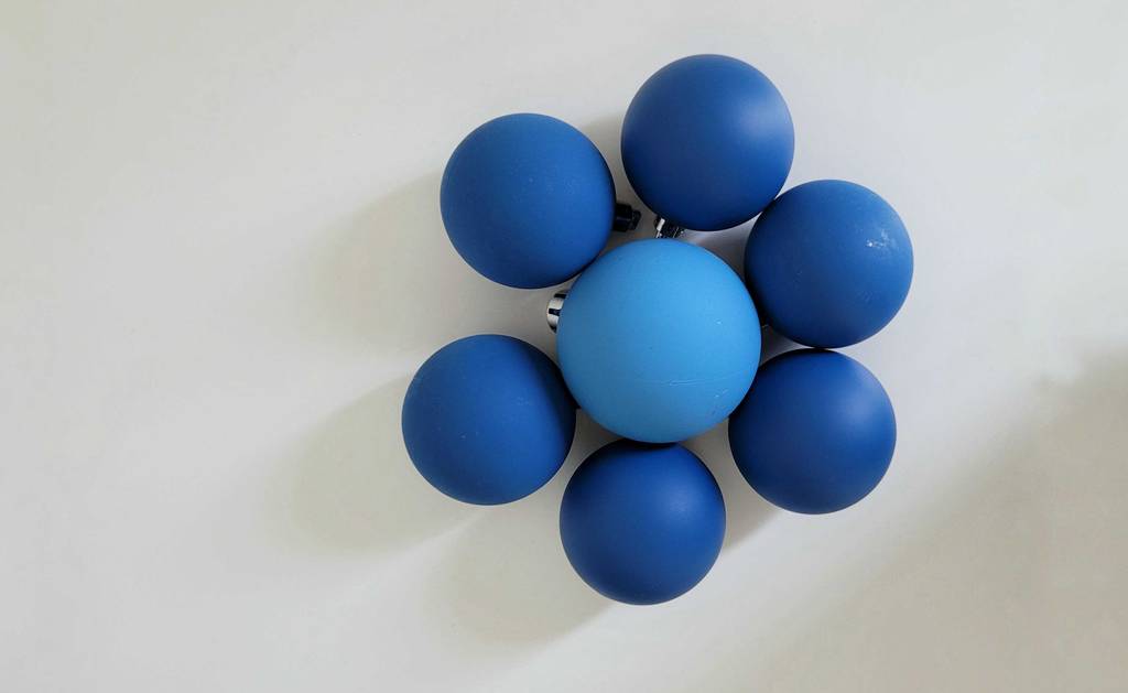 Sieben blaue Weihnachtskugeln liegen zum testen in einer Blumenform angeordnet auf einer weißen Fläche.