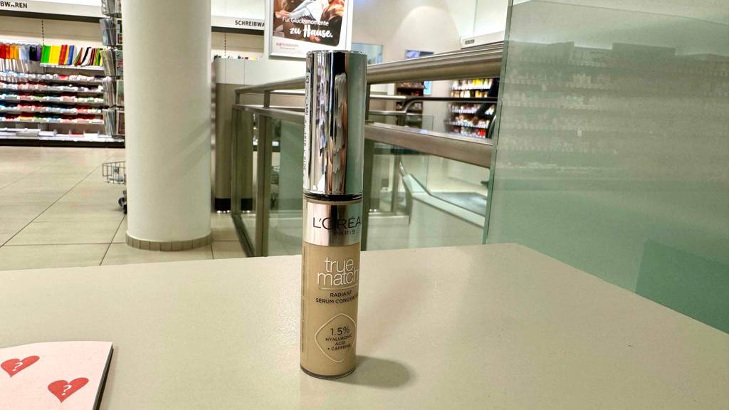 Ein L'Oréal-Concealer im Test steht auf einem beigefarbenen Regalboden in einem Drogeriemarkt.