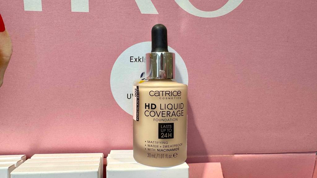 Ein getesteter Catrice-Concealer in der Flasche inklusive Pipette steht vor einem rosafarbenen Hintergrund.