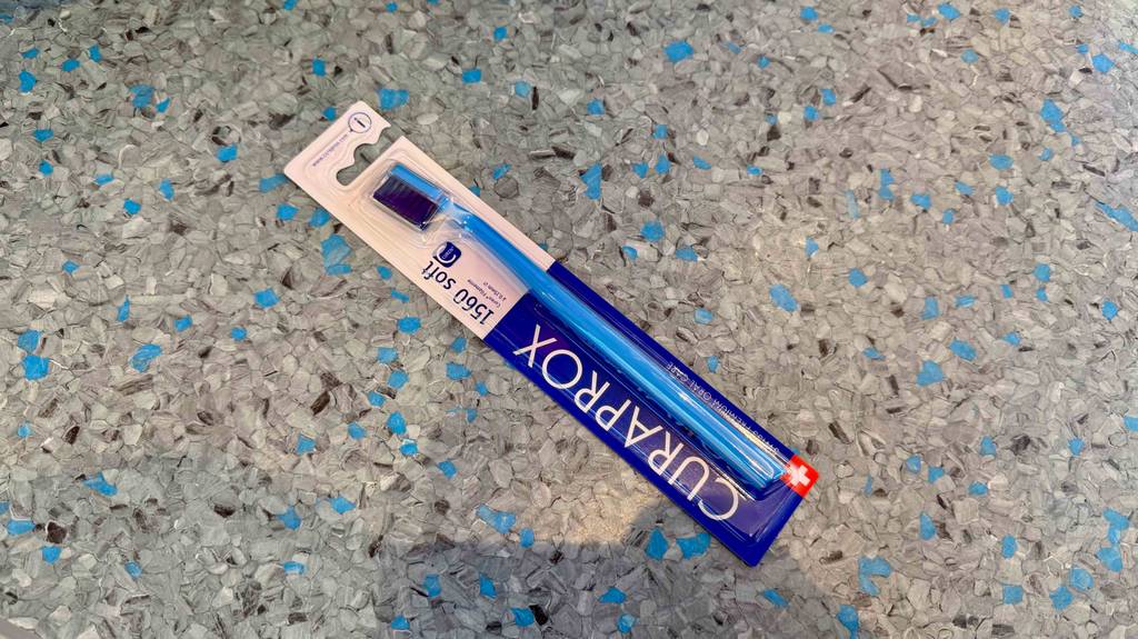 Eine getestete Curaprox-Zahnbürste liegt in ihrer Verpackung auf einem Linoleumbelag.