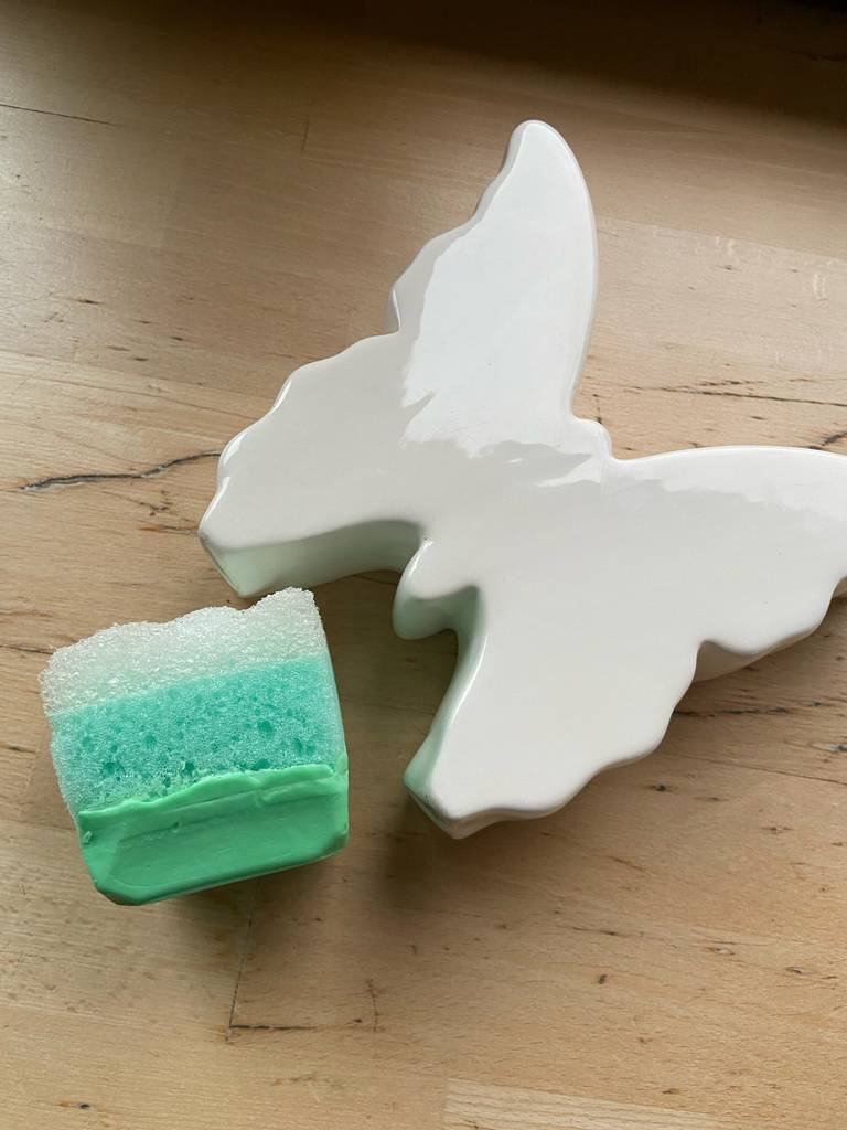 Die grüne Gesichtsseife im Test liegt neben einem weißen dekorativen Schmetterling auf einer Holzoberfläche.