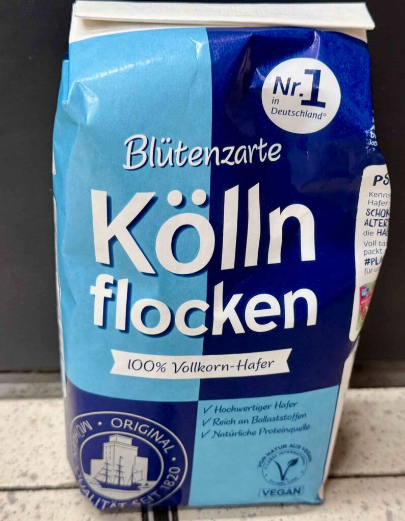 Eine Packung mit Kölln-Haferflocken im Test steht auf einem Fliesenboden vor einer schwarzen Fläche.