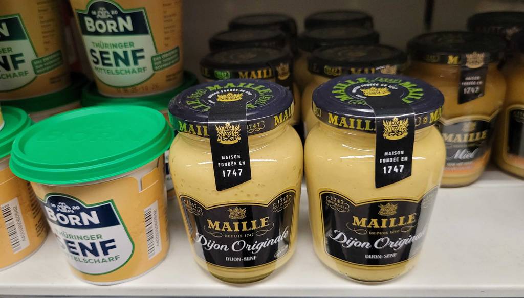 Mehrere Gläser mit getestetem Maille-Senf stehen nebeneinander im Regal eines Supermarktes.