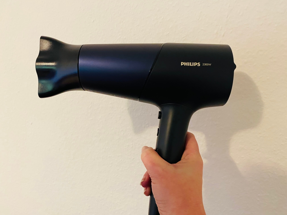 Hier ist der Philips 5000 Series Haartrockner, der in der Hand gehalten wird, mit aufgesteckter Stylingdüse zu sehen.