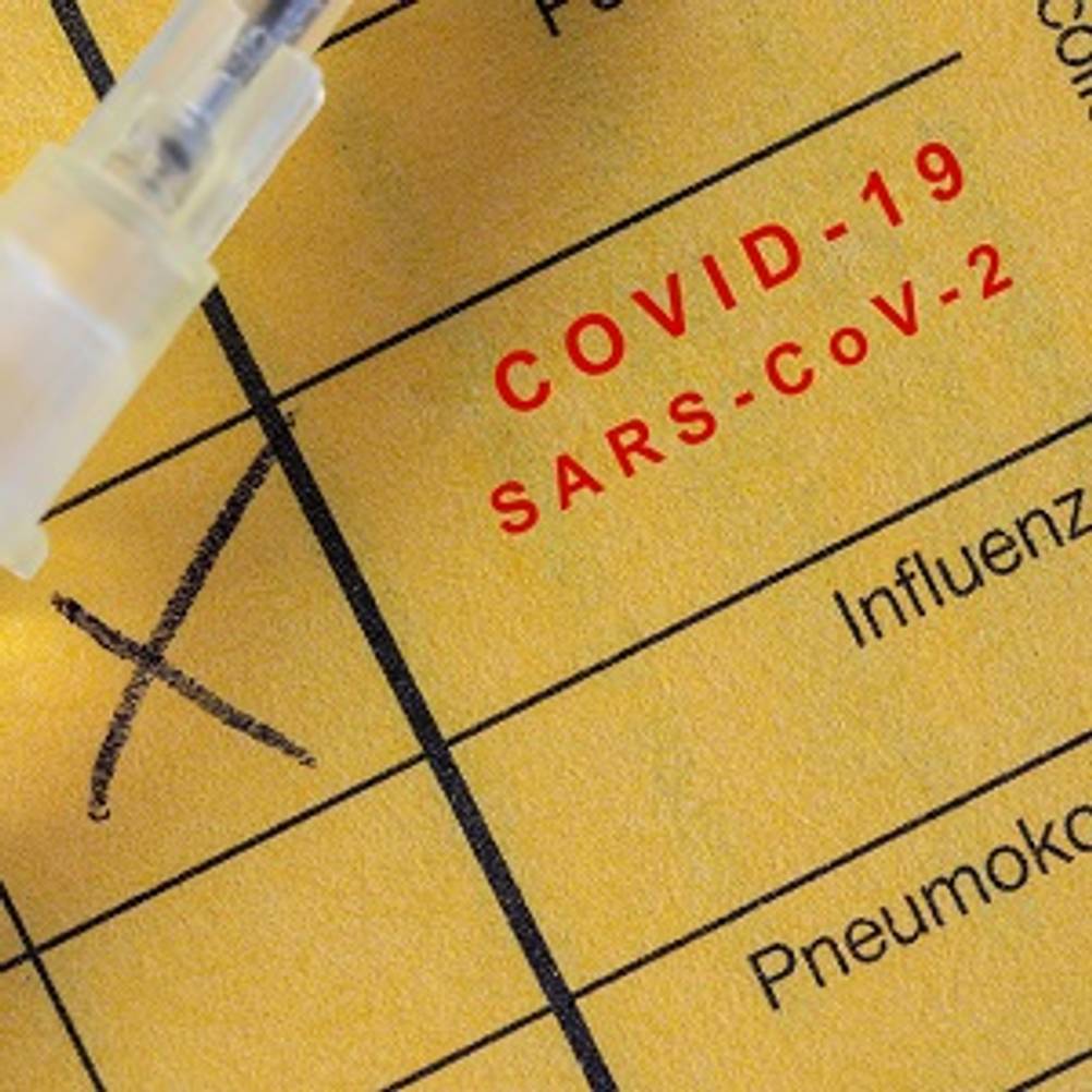 Impfpass getestet: Impfpass mit COVID-19-Impfeintrag, auf dem eine Injektionsspritze liegt. 