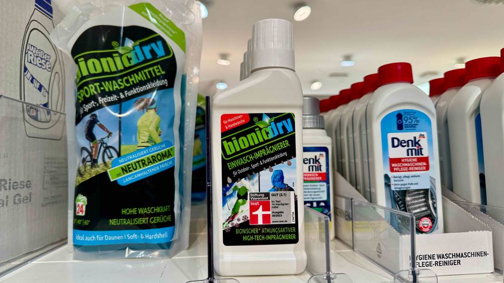 Mehrere Flaschen des getesteten Imprägnier-Waschmittel im Test neben anderen Produkten in einem Verkaufsregal.