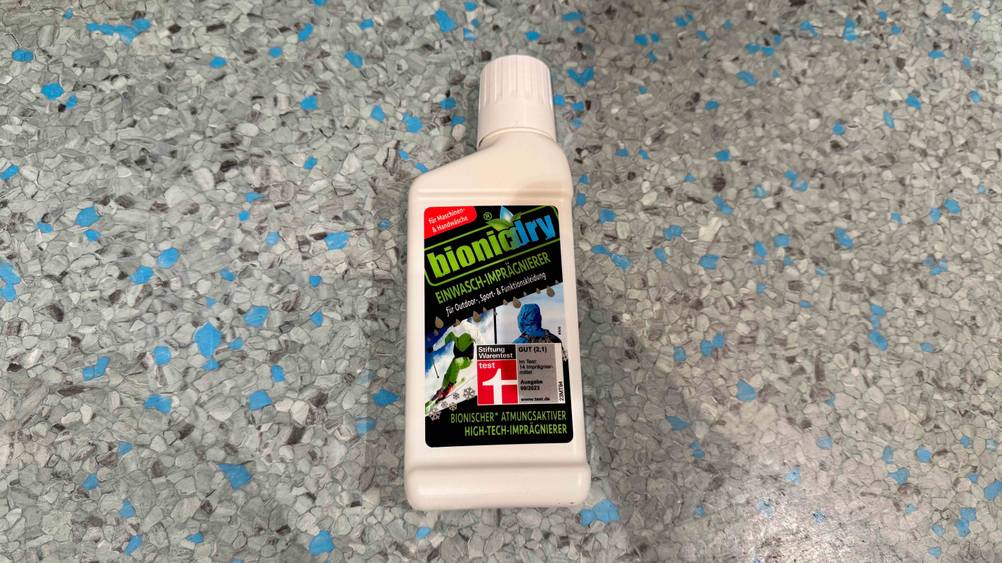Das getestete Imprägnier-Waschmittel liegt auf einem grauen Boden.