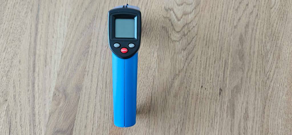 Ein Infrarot-Thermometer liegt mit dem Display nach oben zum testen auf einem Holzboden.