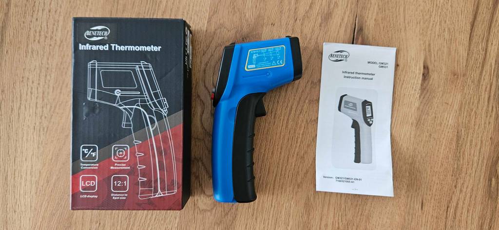 Infrarot-Thermometer im Test: Ein Gerät liegt zwischen Originalverpackung und Anleitung auf einer Holzfläche.