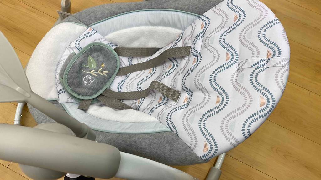 Eine weiß-graue, getestete elektrische Babywippe inklusive Gurtsystem von oben betrachtet.